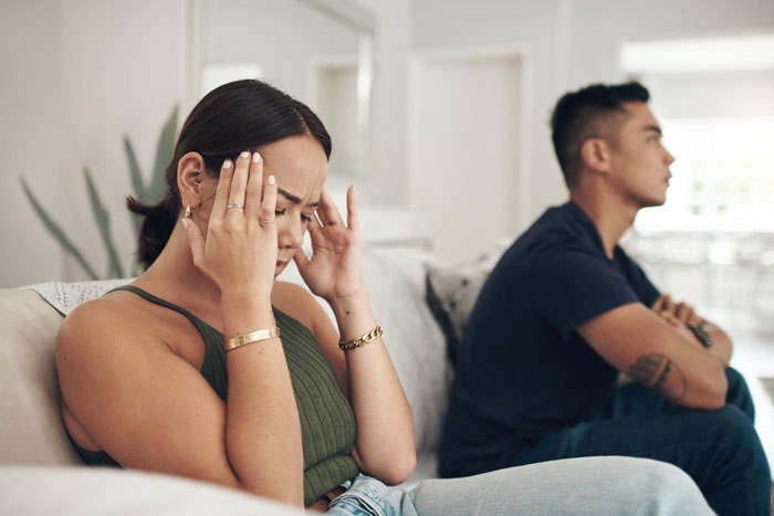 A woman looks stressed with her hands on her head, a man sits turned away, reflecting a SIL who bullies a deaf cousin. A woman looks stressed with her hands on her head, a man sits turned away, reflecting a SIL who bullies a deaf cousin.