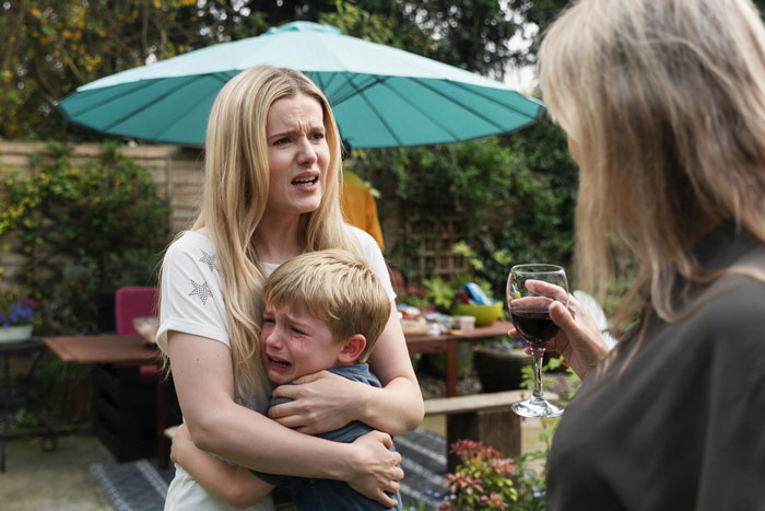 Mother comforting her crying son with an allergy, while his aunt, who triggered his allergy, holds a glass of wine. Mother comforting her crying son with an allergy, while his aunt, who triggered his allergy, holds a glass of wine.