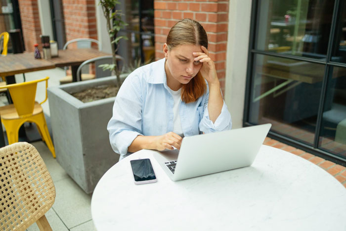 Woman in a cafe, looking stressed at her laptop, showing the infertility and adoption situation.