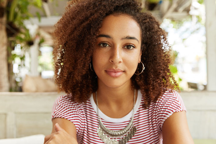 A woman with curly hair looks at the camera, symbolizing the woman discussing her infertility journey.
