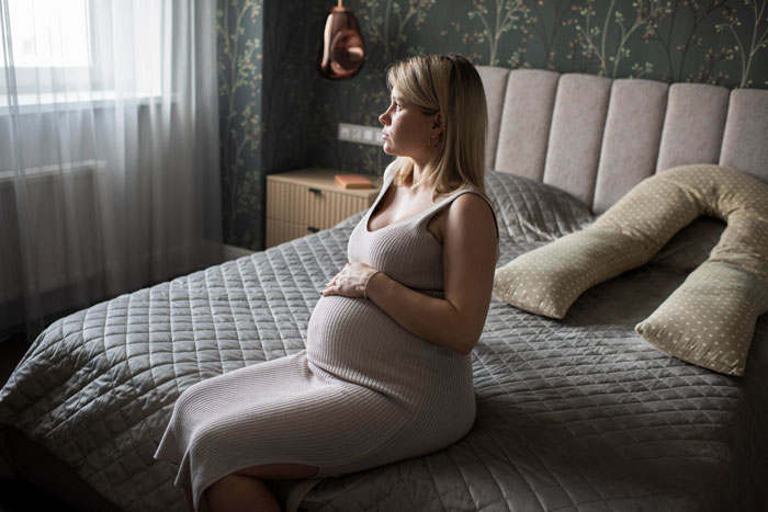 A pregnant woman sits on a bed, illustrating the story of a half-sis taunting woman over infertility and her baby.