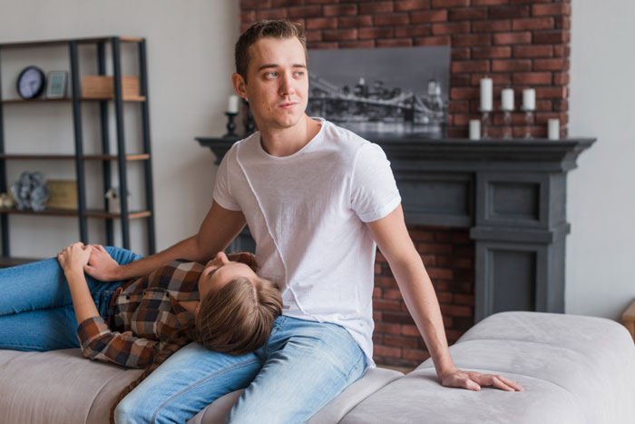 A woman rests her head on a man's lap on a sofa, in a scenario involving a half-sister's taunts over infertility and motherhood.