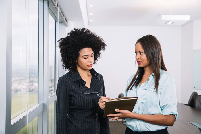 Two professional women in an office, one with curly hair, discussing documents, relating to the half-sis infertility story.
