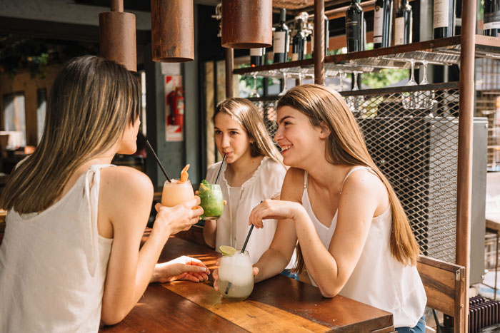 Three young women enjoying drinks at a bar, reflecting on a half-sister's taunts and infertility. Woman as a great mom.