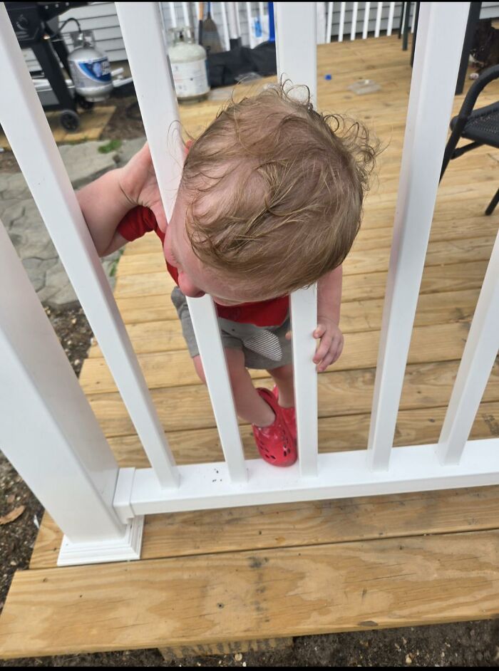 A small child stuck between deck railings, demonstrating a parent's wrong way to ensure safety.