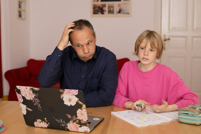 A frustrated father with his hand on his head, looking at his child who is doing homework. This illustrates the struggles of a horrible parent.
