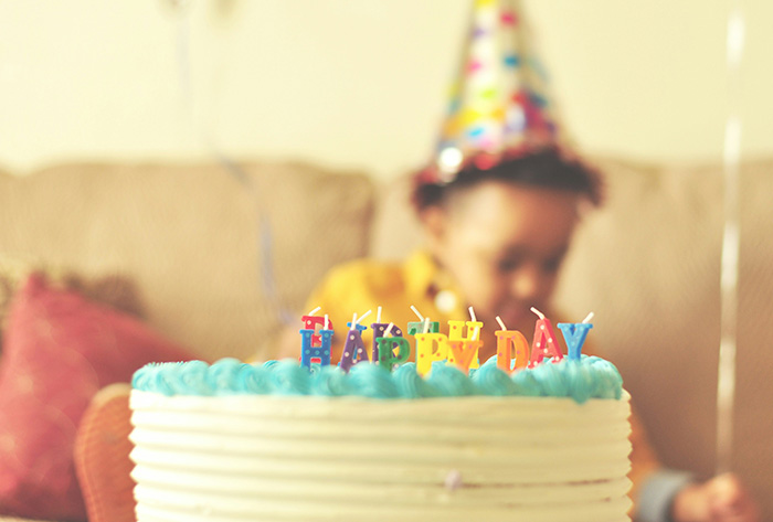 A blurred child in a party hat behind a first birthday cake with Happy Birthday candles, as parents move across country. A blurred child in a party hat behind a first birthday cake with Happy Birthday candles, as parents move across country.
