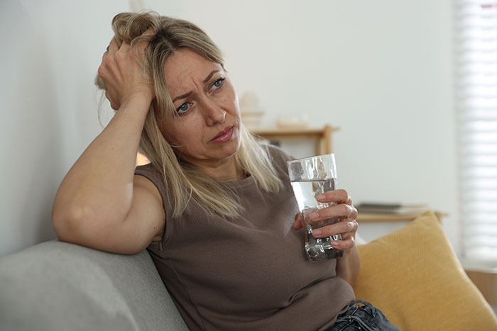 A woman who retires hoping to experience motherhood through grandkids, looks sad and holds a glass of water. A woman who retires hoping to experience motherhood through grandkids, looks sad and holds a glass of water.