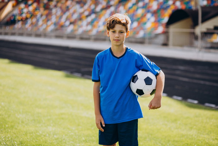 A young boy in a blue soccer uniform holding a ball, representing the son whose sports fees are causing a relationship conflict. A young boy in a blue soccer uniform holding a ball, representing the son whose sports fees are causing a relationship conflict.