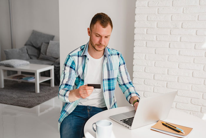 A man, paying for dinners, bills, and gas, looks at his laptop with a credit card, considering his girlfriend's son's sports fees. A man, paying for dinners, bills, and gas, looks at his laptop with a credit card, considering his girlfriend's son's sports fees.