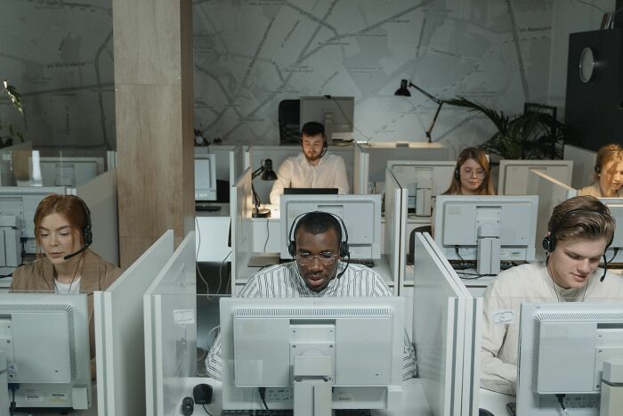 Call center employees wearing headsets, working at computers in a busy office, experiencing workplace dramas