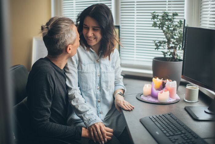 Two women smiling at each other at a desk with candles, showing potential workplace dramas