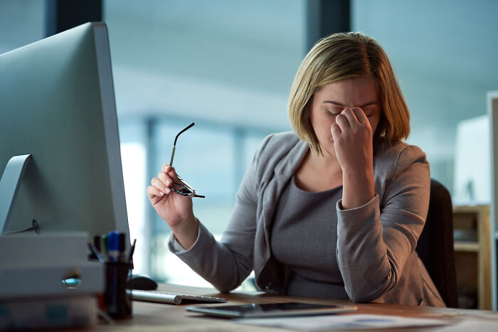A woman sitting at a desk, looking stressed and holding her head, reflecting common work drama scenarios.