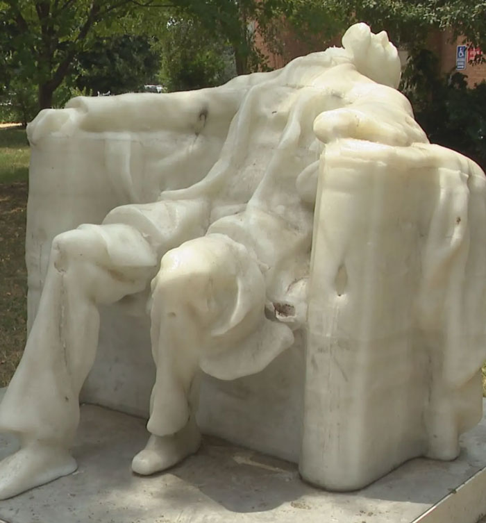A white marble statue of a person sitting in a chair appears to be melting, showing the effects of summer heat.