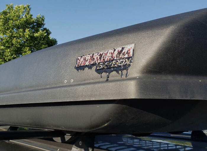 A vehicle's roof cargo box has a sticker that is visibly melted and dripping from the severe summer heat, displaying summer ruining everything.