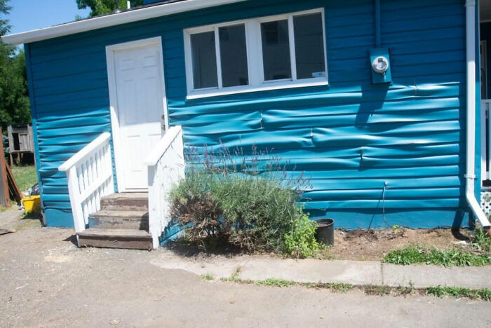 The blue siding of a house appears buckled and melted from the intense summer heat, demonstrating summer ruining everything.