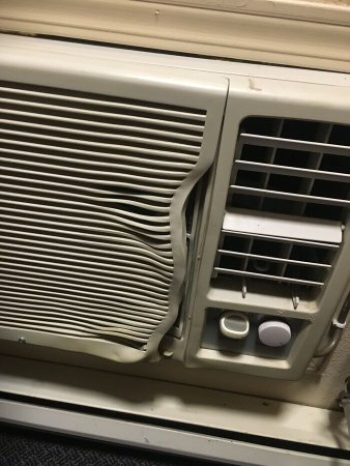 A window air conditioner with its plastic grille partially melted and warped, showing summer ruining appliances.