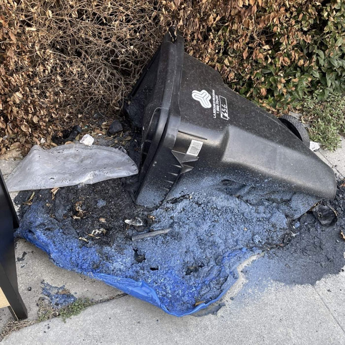 Black trash can overturned next to a puddle of melted blue plastic, ruined by summer temperatures.