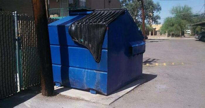 Large blue dumpster with a partially melted and ruined black lid, demonstrating summer damage.