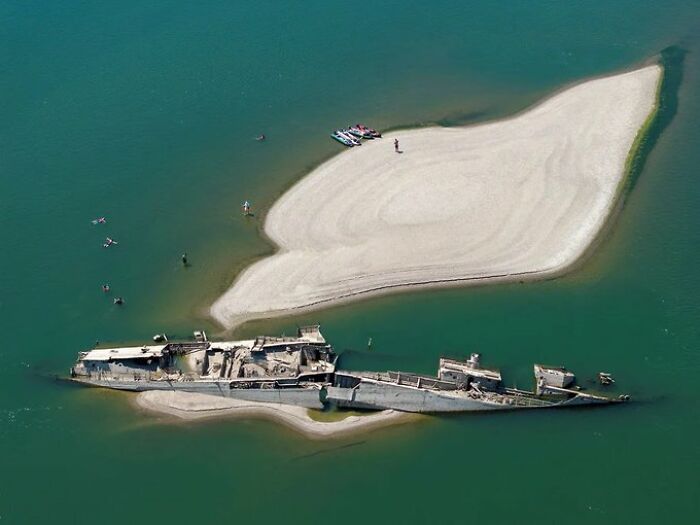 Aerial view of a shipwreck next to a small sandy island, showing summer ruining everything.