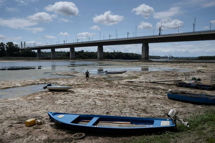 A riverbed showing the effects of summer melting, with boats grounded and cracked earth under a bridge.