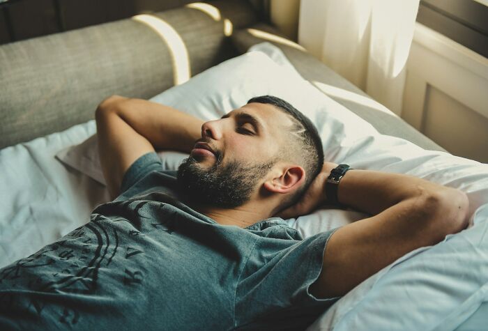 A bearded man sleeps soundly in bed, experiencing a moment of complete freedom during college life.