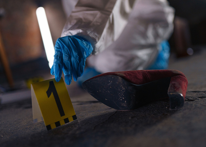 Forensic investigator collecting evidence, a red high heel shoe, after the woman lost her life. Forensic investigator collecting evidence, a red high heel shoe, after the woman lost her life.