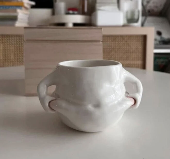 A white ceramic mug with hands grabbing its sides, demonstrating disturbing levels of skill for an awful idea.