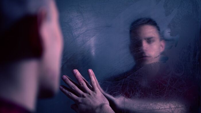 A person touching a foggy mirror, reflecting a blurred face, illustrating the complex nature of mental health disorders.