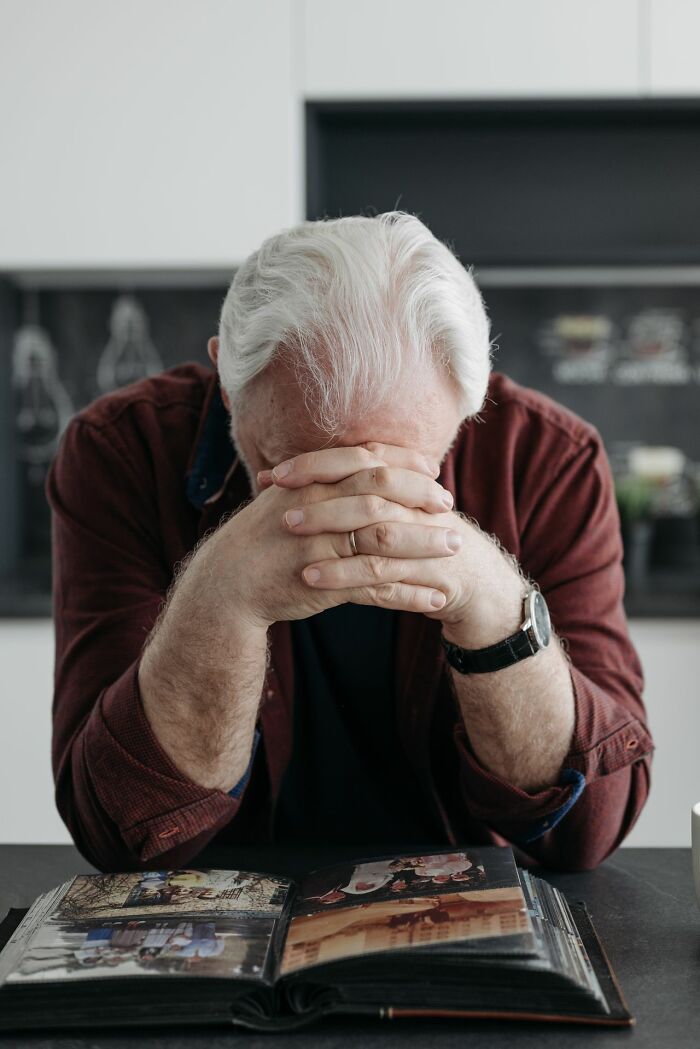 An older man with his head in his hands over a photo album, depicting emotional distress from mental health disorders.