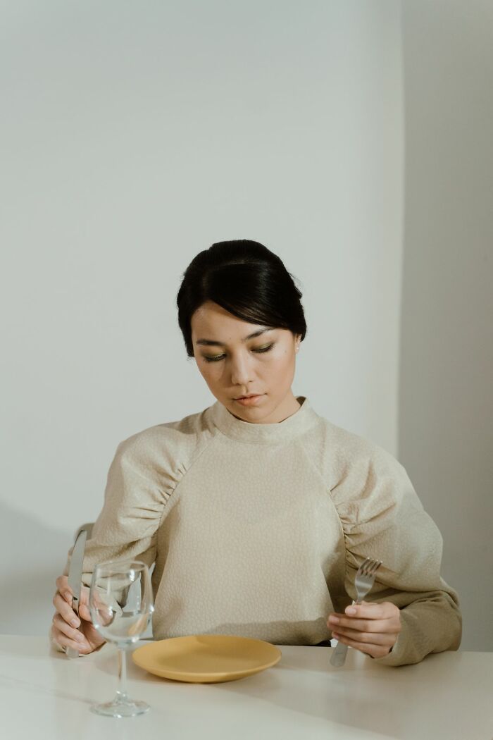 A woman looking down at an empty plate while holding a knife and fork, representing mental health disorders.