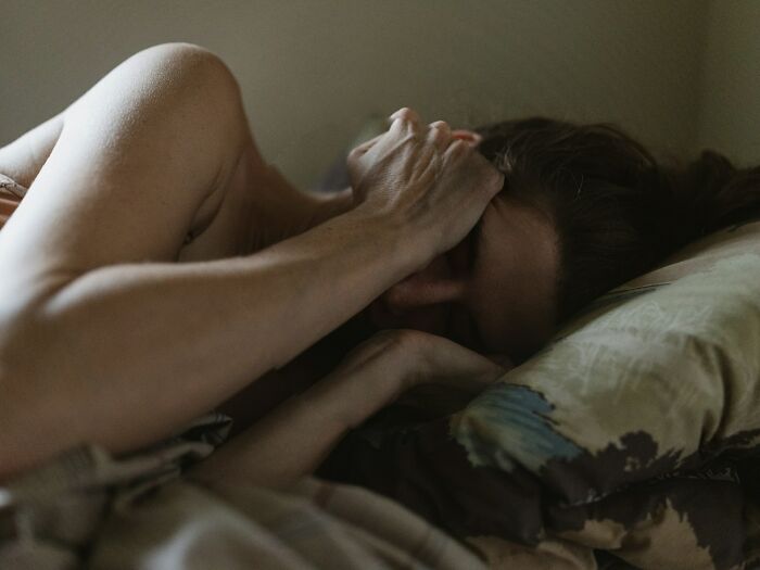 A person with their arm over their face, lying in bed, illustrating the impact of mental health disorders.