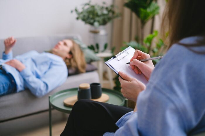 A mental health provider takes notes while a patient lies on a couch in a therapy session for mental health disorders.