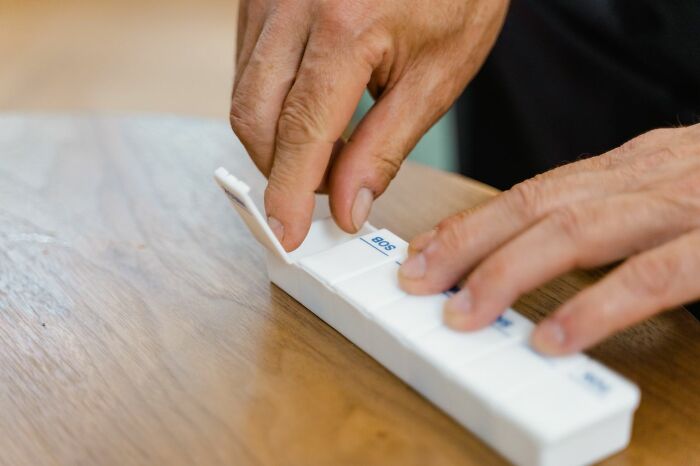 Hands open a pill organizer, showing medication management for treating mental health disorders.