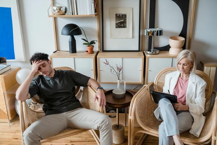 A man looking distressed in a chair next to a mental health provider, illustrating challenges in treating mental health disorders.