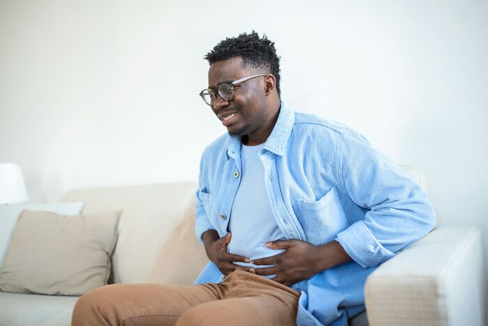 A man sitting on a sofa, clutching his stomach, illustrating physical symptoms related to mental health disorders difficult to treat.
