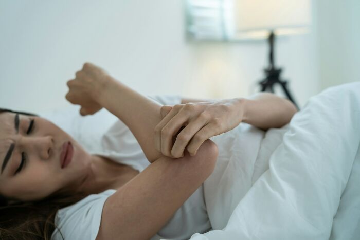 A woman scratching her arm in bed, symbolizing the uncomfortable symptoms of mental health disorders.