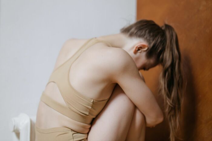 A woman in a beige outfit sitting on the floor with her head down, highlighting the difficulty of treating mental health disorders.
