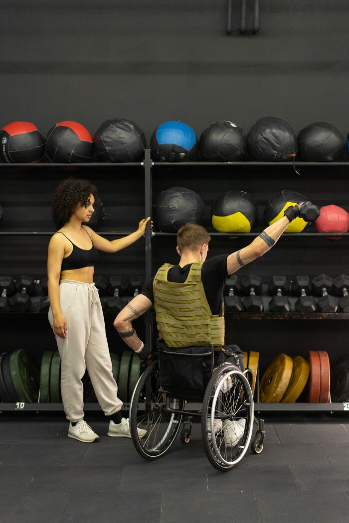 Man in wheelchair lifting weights with a trainer, highlighting inclusion and things America does better.