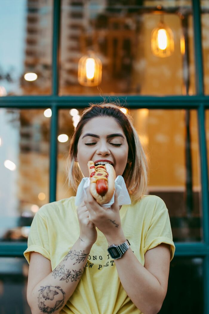 America does better with delicious street food, like a happy woman enjoying a hot dog with condiments.