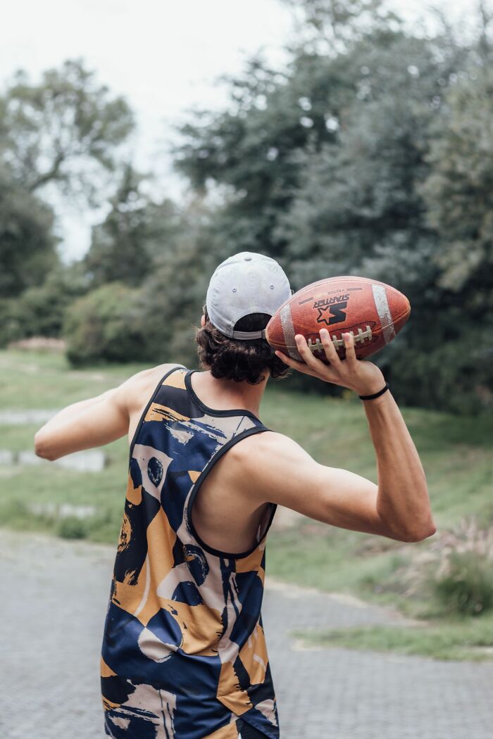 America does better with sports, as a man in a tank top holds a football, ready to throw.