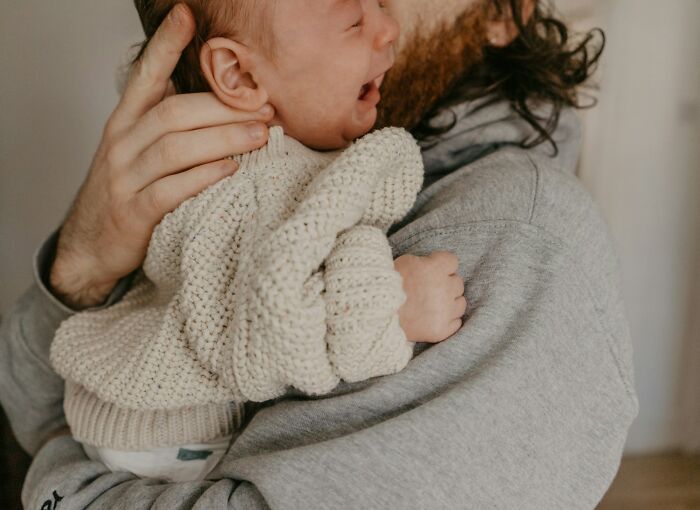 A close-up of a crying baby held by an adult with a beard, symbolizing scary science facts about human vulnerability.