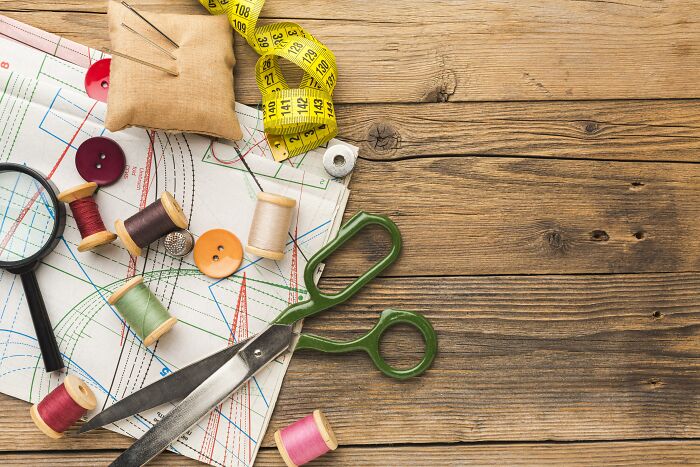 Sewing supplies, including scissors, thread, and a measuring tape, on a wooden table, hinting at unhinged house rules for crafts.