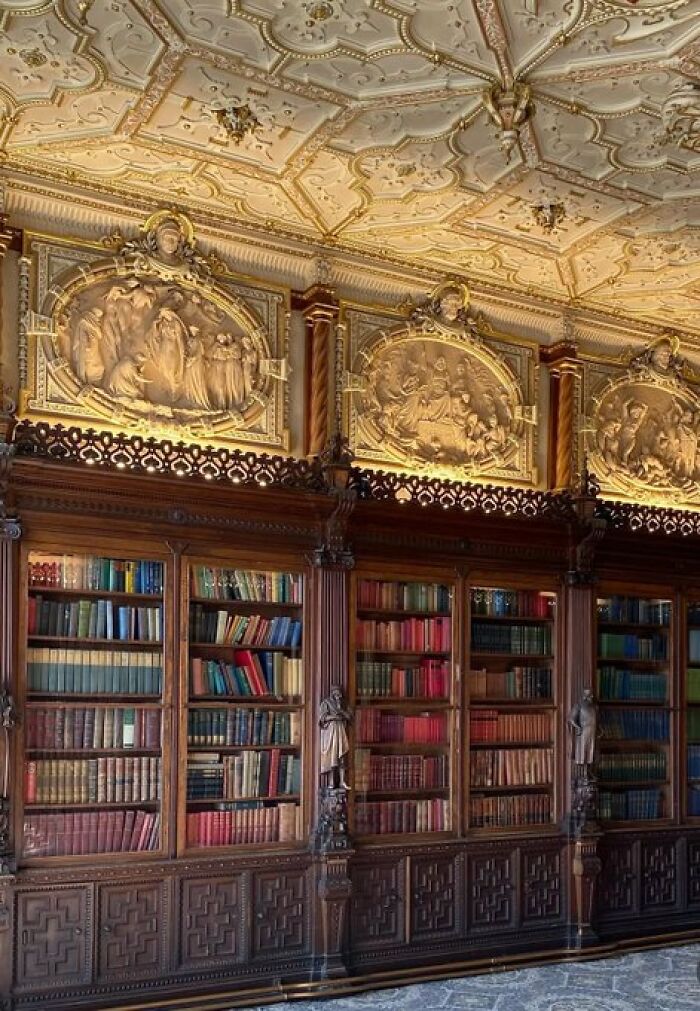 Luxurious library with intricate gold detailing on the ceiling and richly carved wooden bookshelves, highlighting building character.