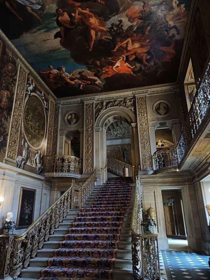 An opulent grand staircase inside a historic building, featuring intricate gold details and a vibrant ceiling mural, full of character.