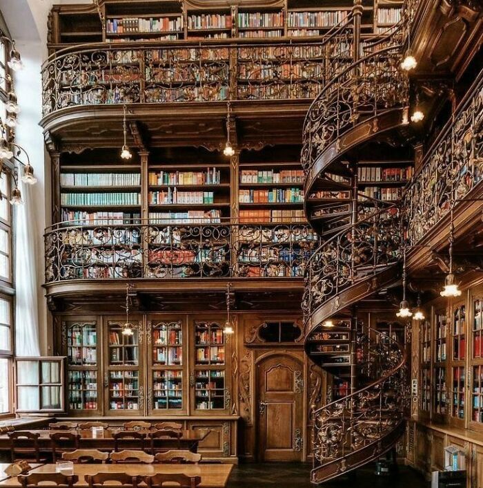 An ornate, multi-story library interior with a spiral staircase, featuring buildings with character in its design.