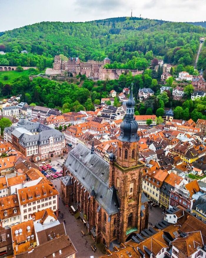 Aerial view of Heidelberg, showcasing buildings with character, a historic castle, and lush green hills.