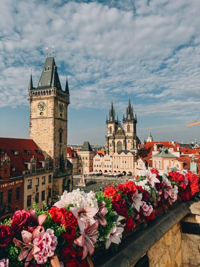 A vibrant city square with historical buildings and a foreground of colorful flowers, showcasing architectural character.