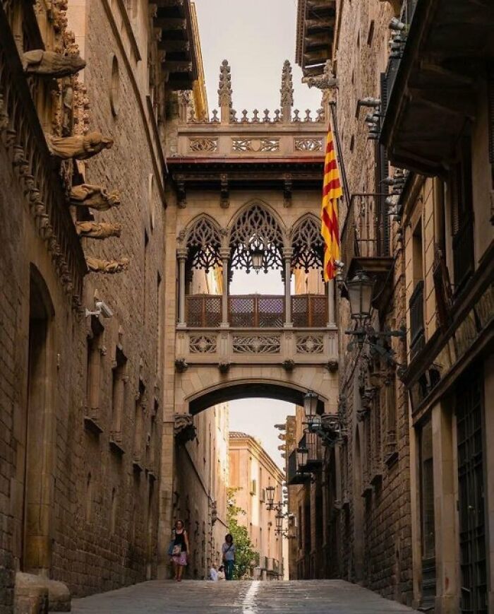Narrow European alleyway with a decorative stone bridge connecting two buildings, highlighting unique architectural character.