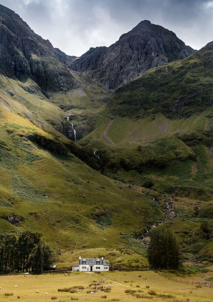 A charming white house nestled in a green valley with majestic mountains and cascading waterfalls, a building with character.